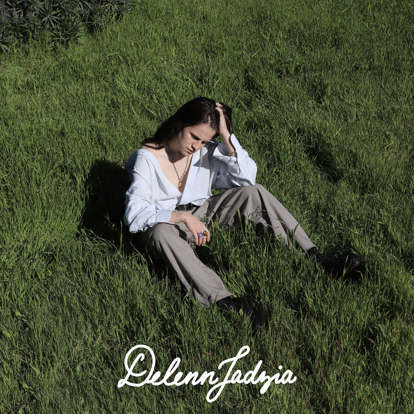 A person in androgynous clothing sits in a grassy field