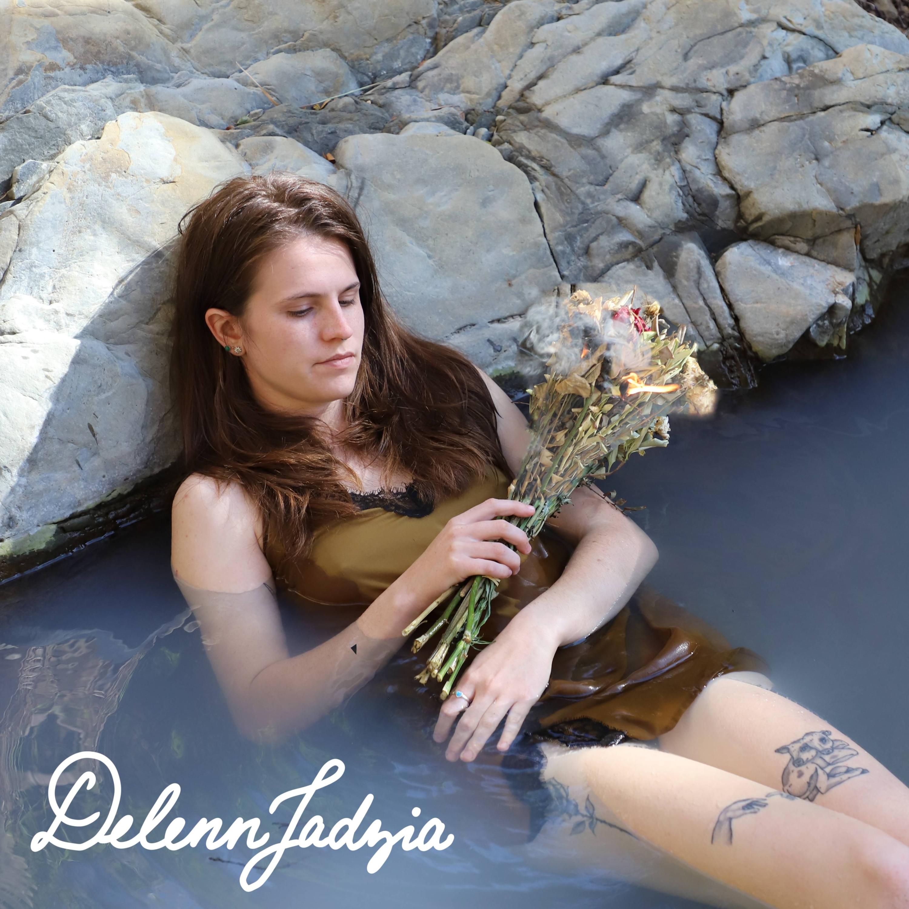 A person in a sild slip is submerged in a spring, holding a flaming bouquet of flowers, reminiscent of Ophelia.